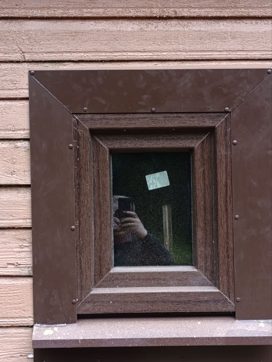 Мале вікно з коричневою металевою обшивкою у дерев’яному будинку